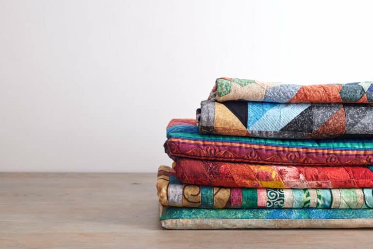 Quilts of different sizes stacked on a wooden table